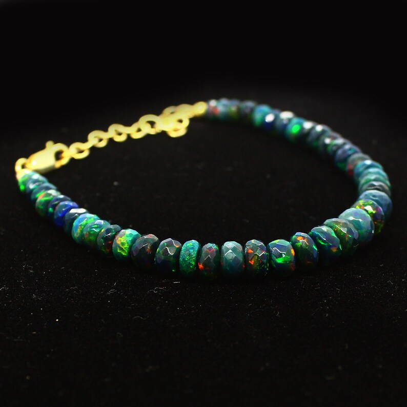 May include: A black opal gemstone bracelet with a gold clasp. The bracelet is made of round, faceted beads that are strung together on a thin chain.