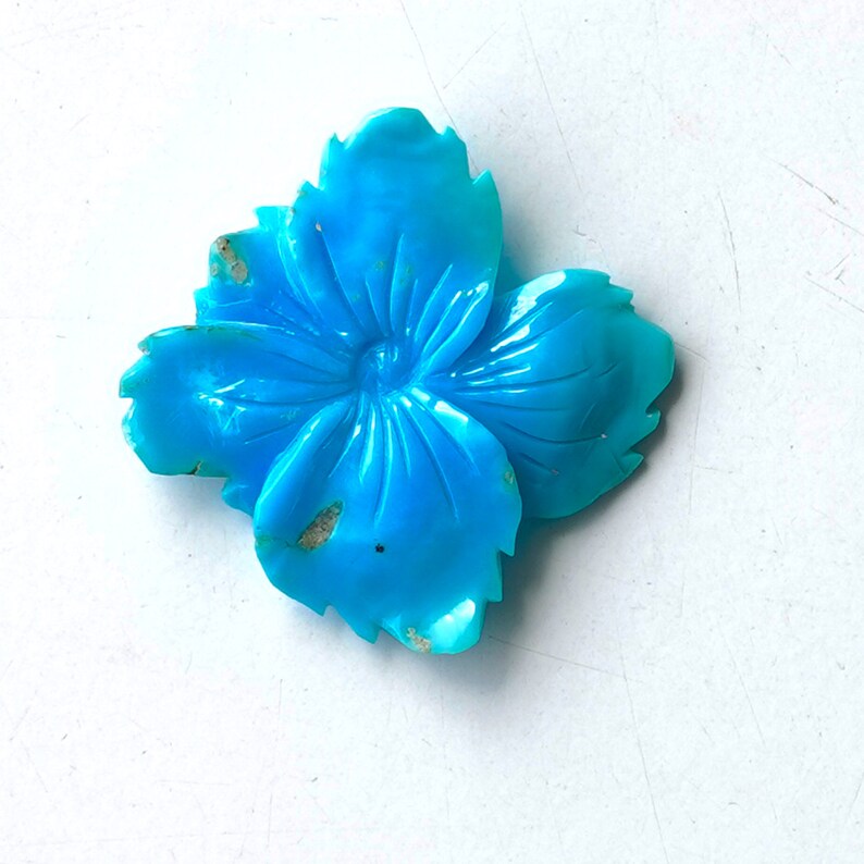 May include: A turquoise blue flower carved from stone. The flower has five petals and a detailed center.