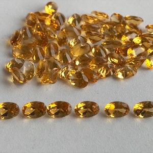 May include: A large pile of oval-shaped, golden yellow gemstones, with a smaller row of seven gemstones in the bottom of the image.