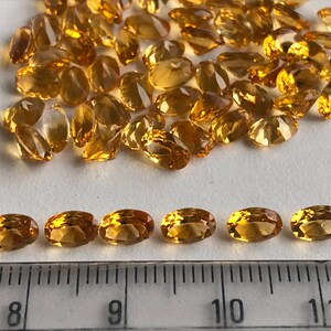 May include: A close-up of a group of oval-shaped, golden yellow gemstones. The gemstones are arranged in a pile, with some of them lined up in a row. A ruler is visible in the bottom of the image, with markings from 8 to 11 inches.