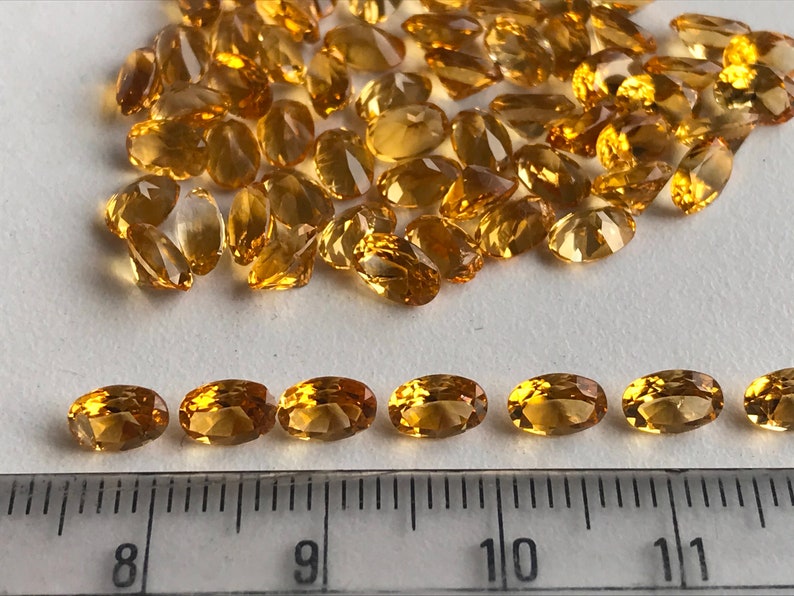 May include: A close-up of a group of oval-shaped, golden yellow gemstones. The gemstones are arranged in a pile, with some of them lined up in a row. A ruler is visible in the bottom of the image, with markings from 8 to 11 inches.
