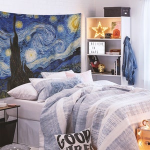May include: A bedroom with a white bed with blue and white striped bedding and a white headboard. The bed has a blue and white throw pillow with the words "Good Vibes" on it. There is a white bookshelf with a star-shaped light, a sign that says "Believe in Naps", and books on the shelves. There is a blue and white tapestry on the wall behind the bed that depicts a starry night sky.