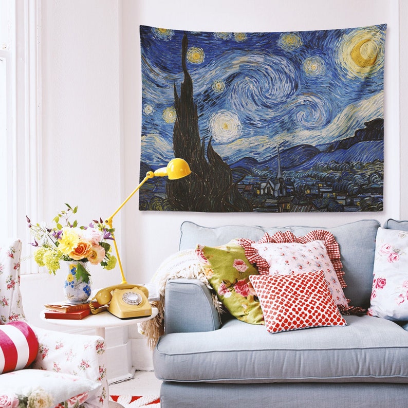 May include: A blue and yellow tapestry featuring a swirling night sky with stars and a crescent moon. The tapestry is hanging on a white wall above a light blue sofa with colorful throw pillows.