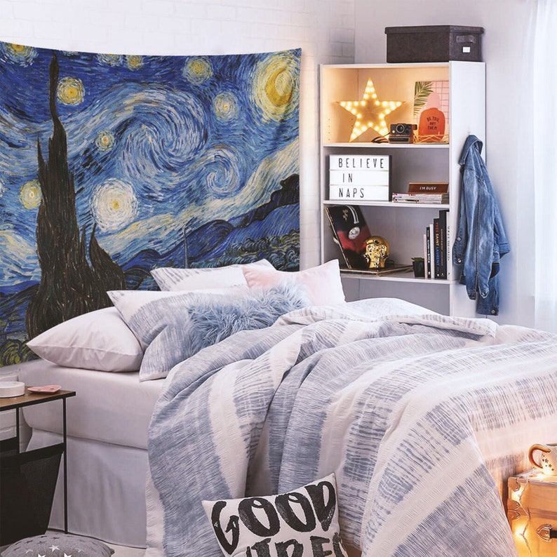 May include: A bedroom with a white bed with blue and white striped bedding and a white headboard. The bed has a blue and white throw pillow with the words "Good Vibes" on it. There is a white bookshelf with a star-shaped light, a sign that says "Believe in Naps", and books on the shelves. There is a blue and white tapestry on the wall behind the bed that depicts a starry night sky.