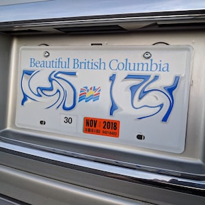 May include: A white license plate with blue text reading "Beautiful British Columbia." The plate features a stylized design and a small Canadian flag. An orange sticker shows "NOV 2018."