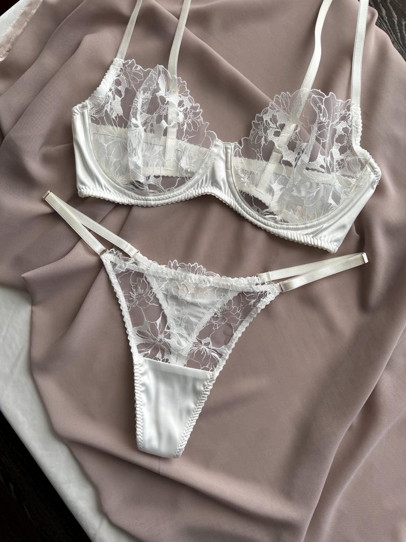 Peut inclure: Ensemble de lingerie en dentelle blanche avec un motif floral d&eacute;licat. Le soutien-gorge a des bretelles r&eacute;glables et une bordure en satin. La culotte assortie est de style string avec un dos en satin.