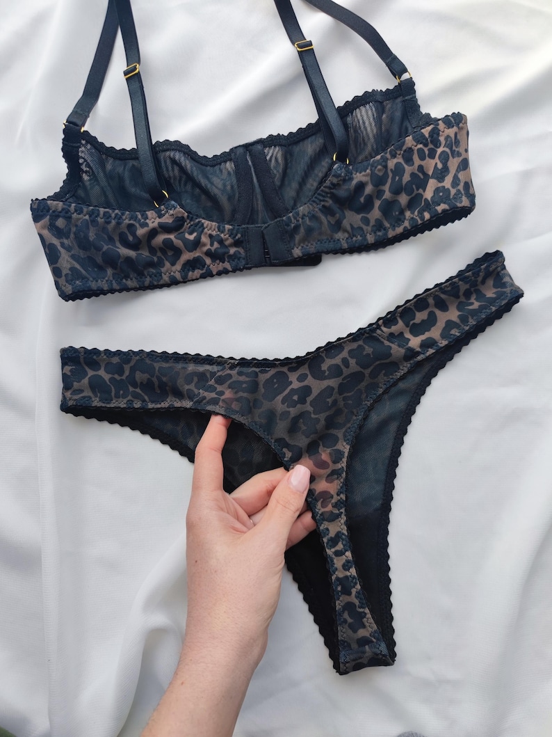 May include: A matching lingerie set featuring a bra and thong. The set is made of a sheer fabric with a leopard print pattern in shades of brown and black. The bra has adjustable straps and a hook-and-eye closure. The thong has a scalloped edge.