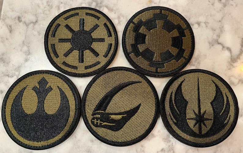 Peut inclure: Six patchs ronds brod&eacute;s avec diff&eacute;rents logos de Star Wars. Les patchs sont noirs et verts sur un fond beige.