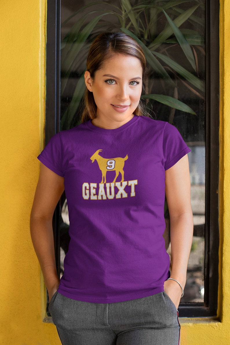 May include: Purple t-shirt with a gold silhouette of a goat wearing a jersey with the number 9. The text "GEAUX" is printed below the goat.