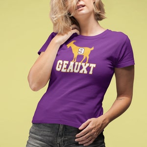 May include: Purple t-shirt with a gold silhouette of a goat with the number 9 on it and the text "GEAUX'T" underneath.