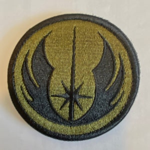 Peut inclure: Un &eacute;cusson brod&eacute; vert et noir avec un sabre laser stylis&eacute; et des ailes. L'&eacute;cusson est circulaire et a une bordure noire.