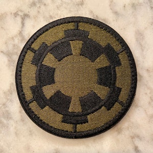 Peut inclure: Un &eacute;cusson rond brod&eacute; de couleur verte et noire repr&eacute;sentant le symbole imp&eacute;rial de Star Wars.