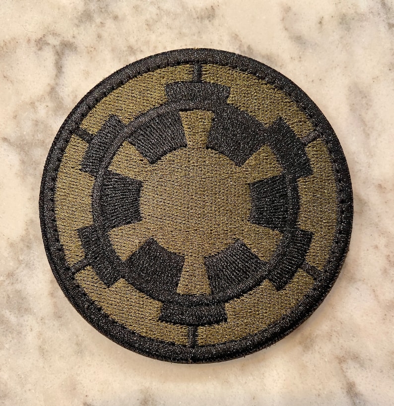 Peut inclure: Un &eacute;cusson rond brod&eacute; de couleur verte et noire repr&eacute;sentant le symbole imp&eacute;rial de Star Wars.