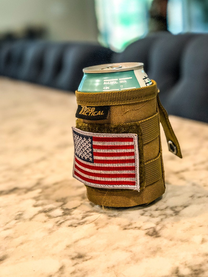 Puede incluir: Un portavasos t&aacute;ctico de color marr&oacute;n claro con un parche de velcro de la bandera estadounidense y el texto "75B Tactical" en la parte delantera. El portavasos contiene una lata de cerveza con el texto "ALCOHOL IBU 4.0% 17" en el lateral.