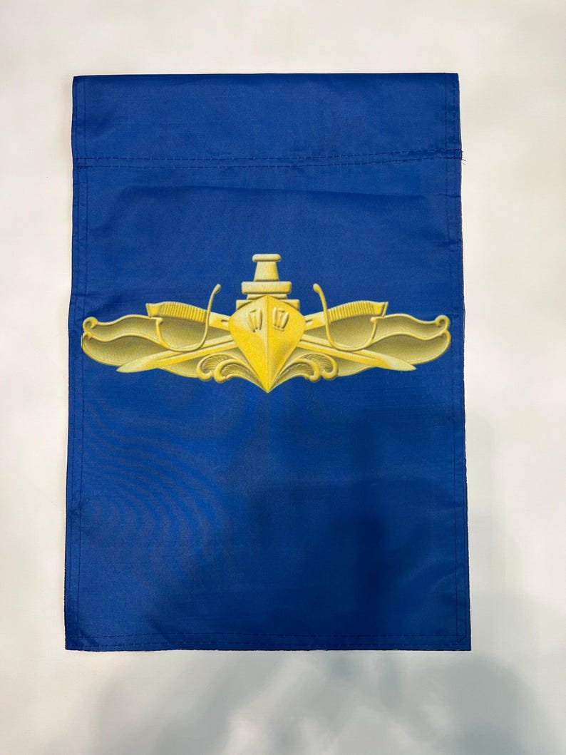 Puede incluir: Una bandera de jard&iacute;n azul con un emblema de submarino dorado. El emblema presenta un submarino con dos delfines flanqueantes y un tridente.