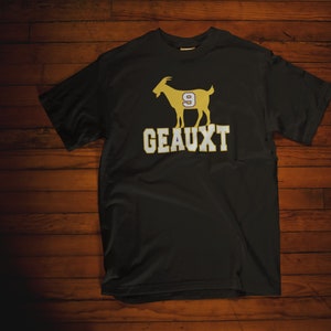 May include: Black t-shirt with a gold silhouette of a goat wearing a jersey with the number 9. The text "GEAUX" is printed below the goat.