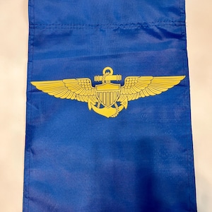 May include: A blue garden flag with a gold embroidered emblem of an anchor and wings. The emblem also includes a shield with a design resembling the American flag.