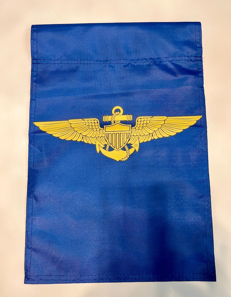May include: A blue garden flag with a gold embroidered emblem of an anchor and wings. The emblem also includes a shield with a design resembling the American flag.