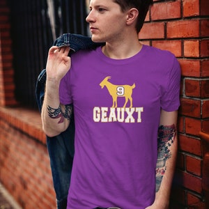 May include: Purple t-shirt with a yellow silhouette of a goat wearing a jersey with the number 9. The text "GEAUX" is printed below the goat.