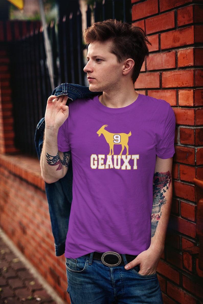 May include: Purple t-shirt with a yellow silhouette of a goat wearing a jersey with the number 9. The text "GEAUX" is printed below the goat.