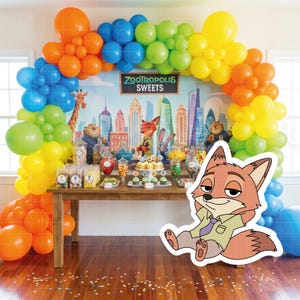 May include: A Zootopia-themed party setup with a wooden table laden with sweets, cupcakes, and candies. A colorful balloon arch frames a backdrop with city skyline and character illustrations. A cutout of Nick Wilde is in the foreground.