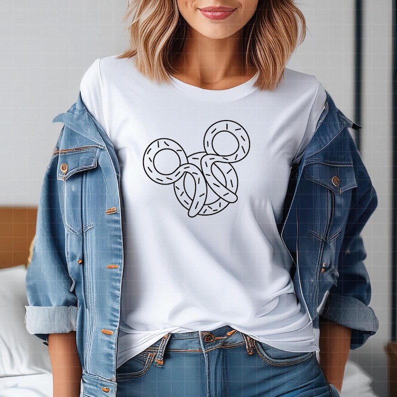 May include: A white short-sleeved t-shirt featuring a black line-art graphic of a pretzel shaped like a mouse head, worn under a blue denim jacket with copper-colored buttons and visible stitching details on the front pockets and seams.