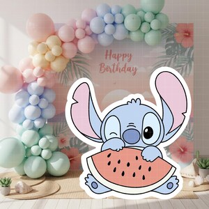 Może przedstawiać: Kresk&oacute;wkowa postać mruga okiem, trzymając kawałek arbuza. Tło przedstawia pastelowy łuk z balon&oacute;w, tło z tropikalnymi kwiatami i napisem "Happy Birthday". Scena rozgrywa się na jasnej powierzchni.