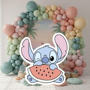 Może przedstawiać: Jasnoniebieska postać z kresk&oacute;wki mrugająca i trzymająca plaster arbuza. Postać ma duże uszy i biały kontur. W tle kolorowy łuk z balon&oacute;w w pastelowych kolorach, z tropikalną scenerią.