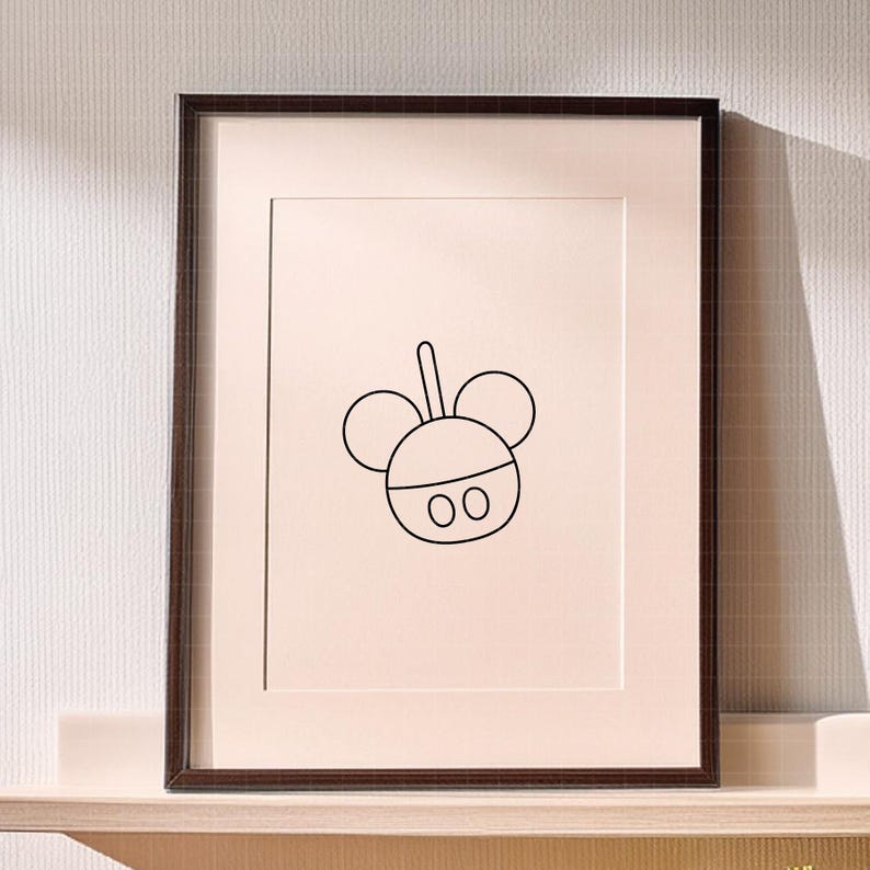 May include: A framed wall art piece featuring a minimalist black line drawing of a stylized mouse head silhouette with two circular ears and two small oval shapes at the bottom, centered on a light cream-colored background within a dark brown frame.