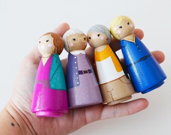 May include: Four wooden peg dolls, each painted to resemble a character. The dolls are dressed in various outfits, including a pink dress with a teal jacket, a purple dress with a belt, a white shirt with an orange shawl, and a blue dress.