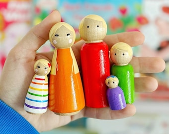May include: A set of five wooden peg dolls, each with a different colored dress or shirt. The dolls are arranged in a row, with the tallest doll on the left and the shortest doll on the right. The dolls have painted faces and blonde hair.