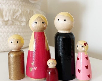 May include: A set of five wooden peg dolls, painted in various colors. The dolls are dressed in pink, red, and black clothing. The dolls have painted faces with black eyes and red lips.