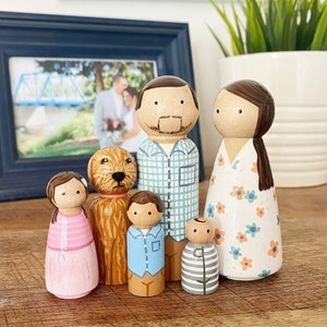 May include: A set of six wooden peg dolls, including a family of four and a dog. The dolls are painted in various colors, including blue, pink, green, and brown. The family members have painted facial features, and the dog has a brown and white coat.