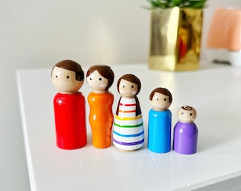 May include: A set of six wooden peg dolls painted in rainbow colors. The dolls are standing in a row on a white surface.