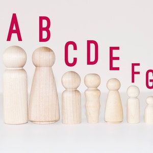 May include: Seven wooden peg dolls of varying sizes, arranged in a line from largest to smallest. The dolls are unpainted and have a natural wood finish. The letters A through G are printed above the dolls in red.