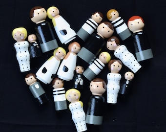 May include: A collection of wooden peg dolls, painted in black, white, and grey with various patterns. The dolls are arranged in a heart shape on a black background.