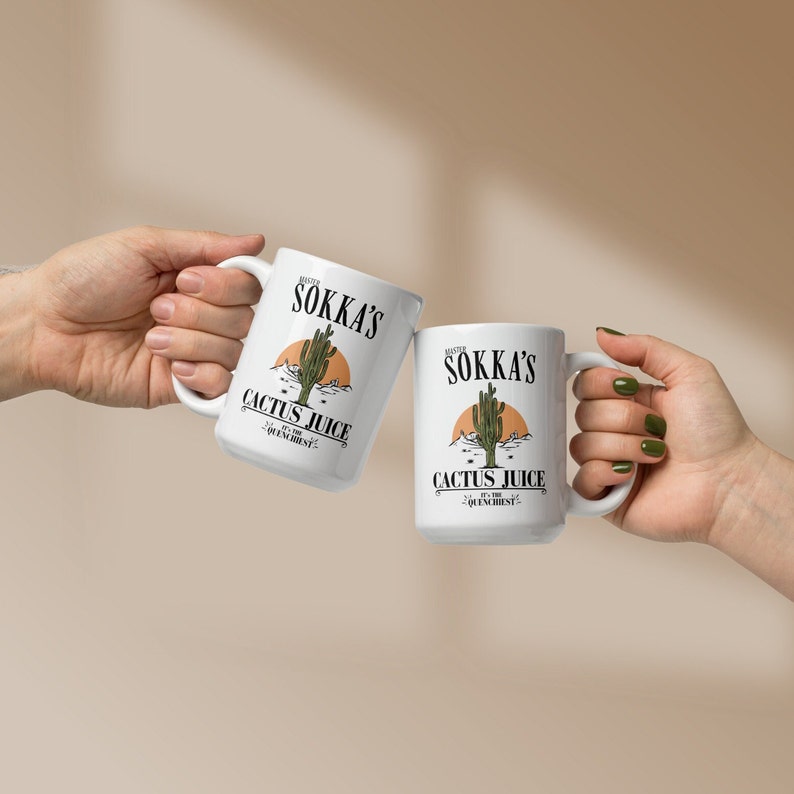 May include: Two white ceramic mugs with the text "Mister Sokka's Cactus Juice" and a desert scene graphic. The mugs are held up in a celebratory gesture, showcasing the design. The mugs are a perfect gift for any occasion.