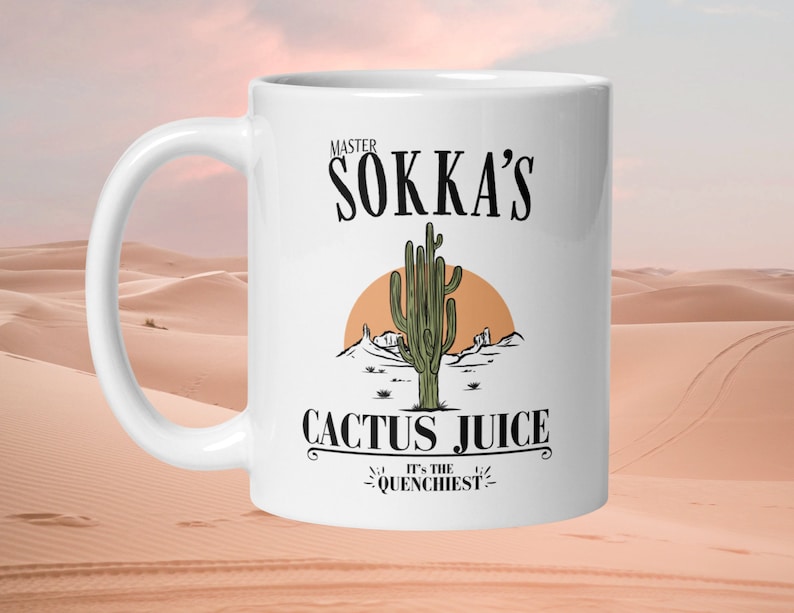 May include: White ceramic mug featuring the text "MASTER SOKKA'S CACTUS JUICE" with a desert landscape illustration. The design includes a cactus, a setting sun, and the phrase "IT'S THE QUENCHIEST".