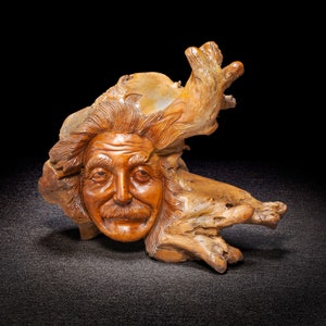 May include: A wooden sculpture of a man's face carved into a piece of driftwood. The sculpture has a whimsical and realistic style.