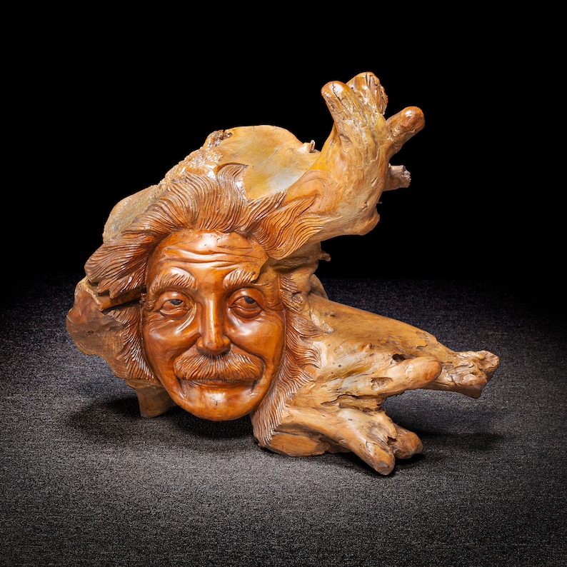 May include: A wooden sculpture of a man's face carved into a piece of driftwood. The sculpture has a whimsical and realistic style.