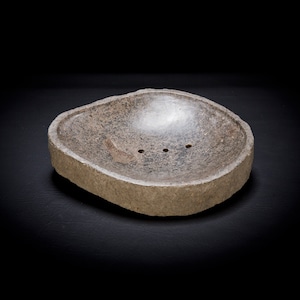 May include: A gray stone soap dish with a rounded, slightly concave interior and three drainage holes.