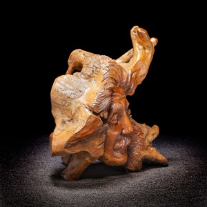 May include: A wooden sculpture of a man's face carved into a piece of driftwood. The sculpture is detailed and realistic, with a weathered look.