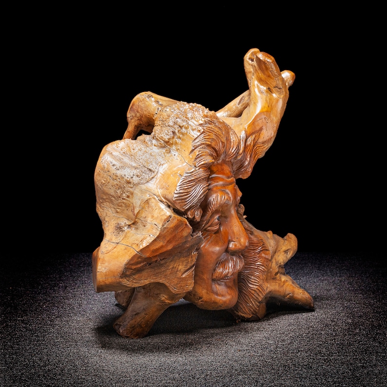 May include: A wooden sculpture of a man's face carved into a piece of driftwood. The sculpture is detailed and realistic, with a weathered look.