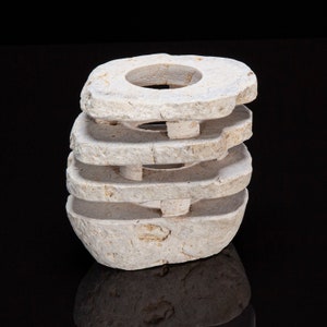 May include: A stack of five white, round, stone rings with a hole in the center of each ring. The rings are stacked on top of each other, creating a decorative object.