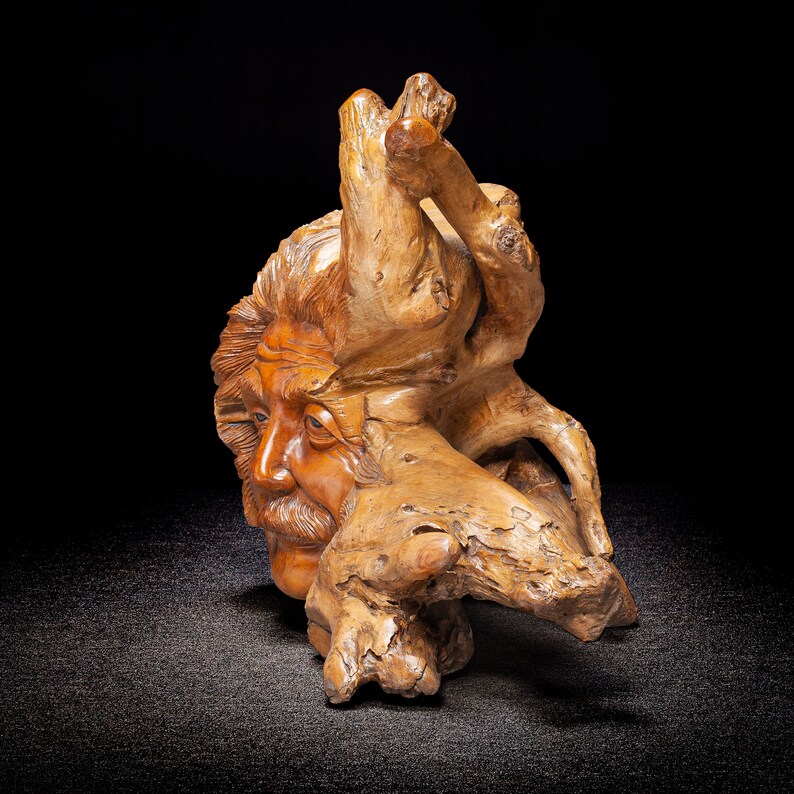 May include: A wooden sculpture of a man's face carved into a tree root. The sculpture is made of natural wood and has a rustic, organic look.