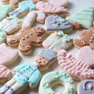 May include: Assortment of Christmas-themed sugar cookies decorated with pastel icing. The cookies feature designs such as a gingerbread man, a Christmas tree, a wreath, a present, and a nutcracker.