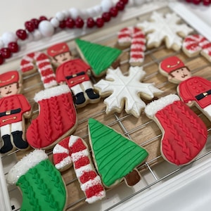 May include: A collection of Christmas-themed sugar cookies decorated with red, green, and white icing. The cookies are shaped like candy canes, Christmas trees, snowflakes, stockings, and nutcrackers.