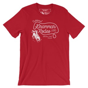 Puede incluir: Camiseta roja con un diseño gráfico blanco que dice "National Grammar Rodeo 1996" con un vaquero montando un caballo que se resbala. El gráfico también incluye el texto "Sheraton Hotel Canada".