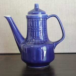 Puede incluir: Una tetera de cerámica azul con tapa blanca y un patrón geométrico. La tetera tiene un pico y una manija.