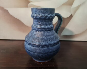 May include: A blue ceramic pitcher with a textured surface and a handle. The pitcher has a rounded body and a wide mouth.